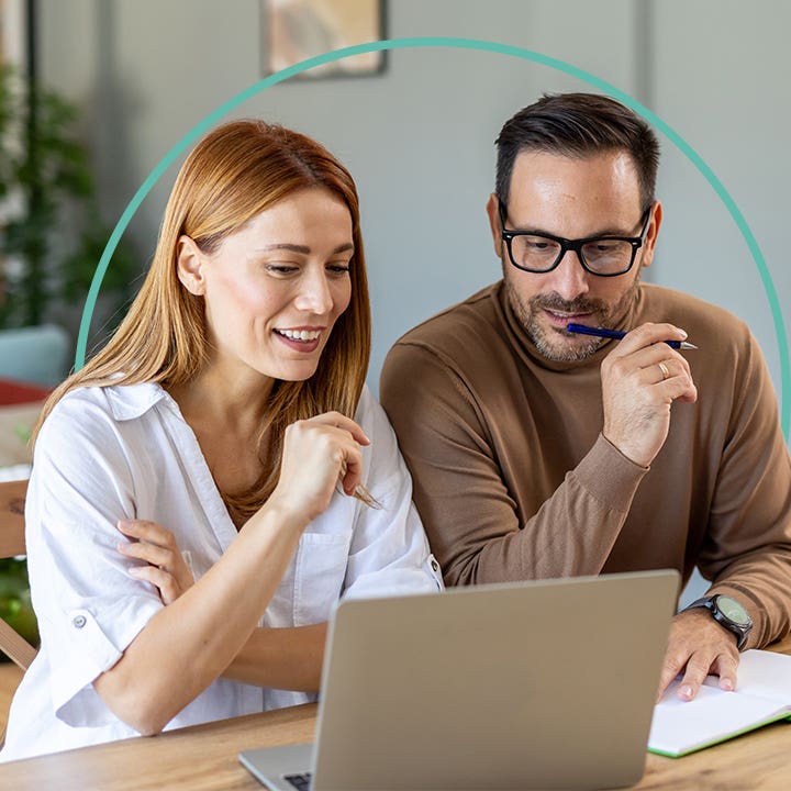 A man and a woman sit at a desk while looking at a laptop.
