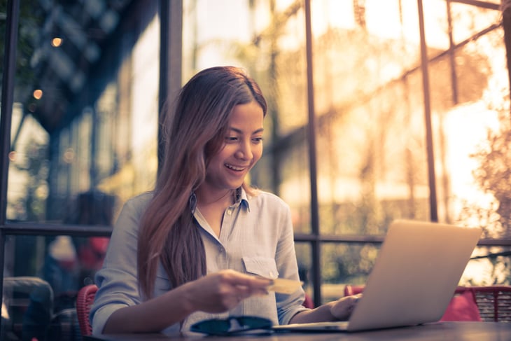 Happy Asian woman on laptop with credit card at coffee shop
